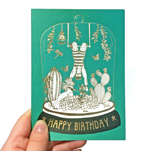 Green birthday card with gold detail featuring an acrobat in a belljar
